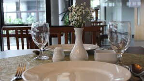 A dining table set with plates, glasses, and a vase of flowers. - Grand Laguna Hotel & Villa (Colomadu)