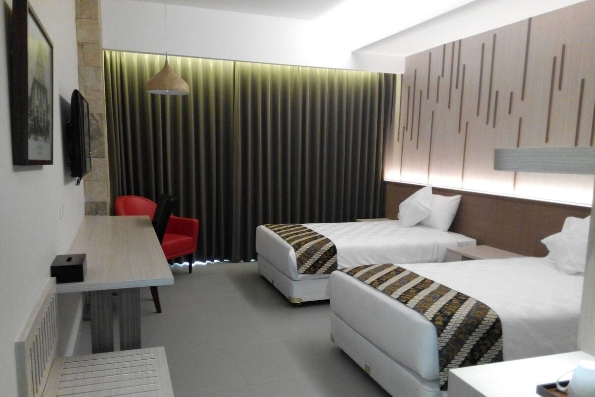 A hotel room with two beds, a desk, a chair, a TV, and a curtain.