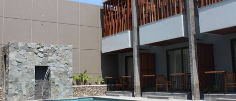 A pool area with a stone wall, wooden deck, and a modern building with balconies.