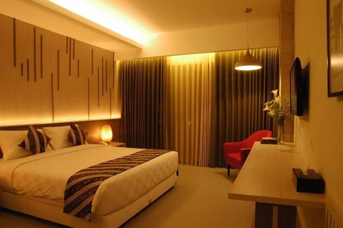 A hotel room with a bed, a desk, a chair, a lamp, and a painting on the wall.