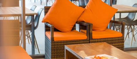 Una silla de mimbre con cojines naranja y una mesa de madera con una revista.
