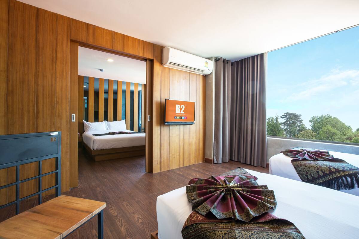 A hotel room with two beds, a TV, an air conditioning unit, and a view of the outdoors.
