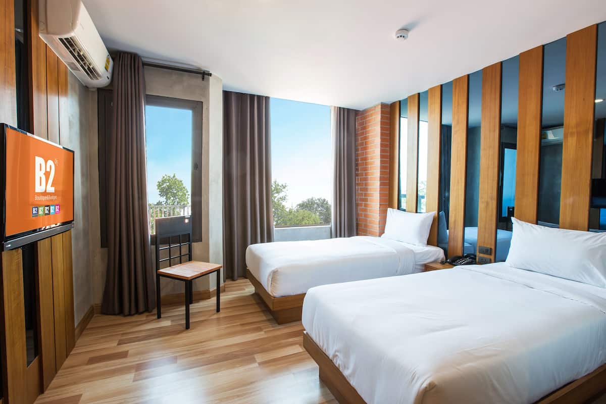 A hotel room with two beds, a TV, a desk, and a view of the outdoors.