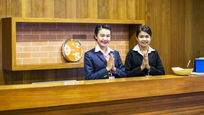 A reception desk with two staff members standing behind it, a clock, and a blue trash bin. - B2 Udon Boutique & Budget Hotel (Udon Thani)