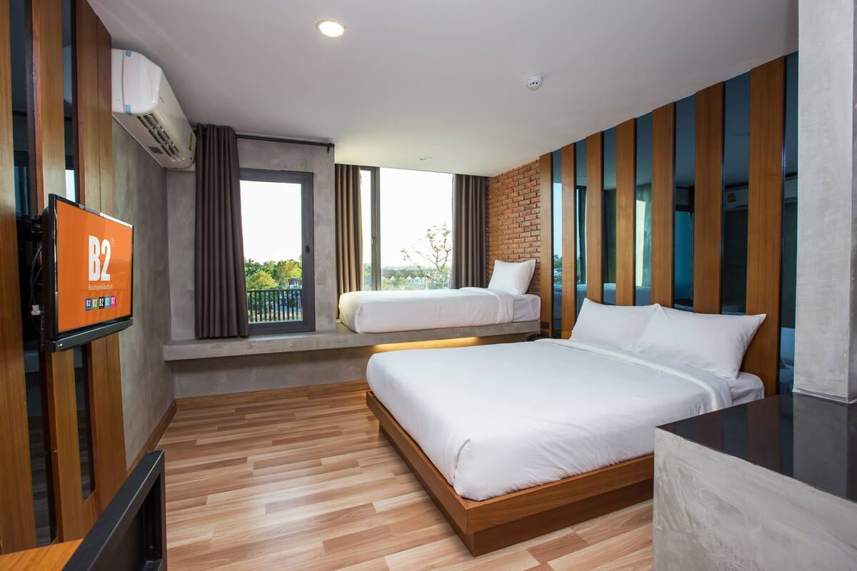A modern hotel room with a large bed, a smaller bed, a TV, and a window with a view.