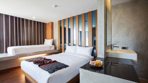 A modern hotel room with a large bed, a bedside table with a bottle, and a bathroom with a sink. - B2 Udon Boutique & Budget Hotel (Udon Thani)