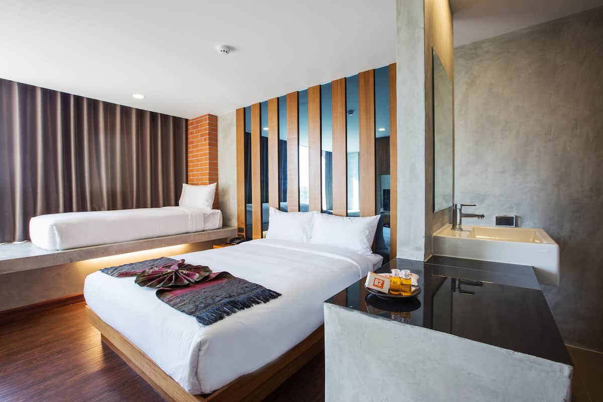 A modern hotel room with a large bed, a bedside table with a bottle, and a bathroom with a sink.