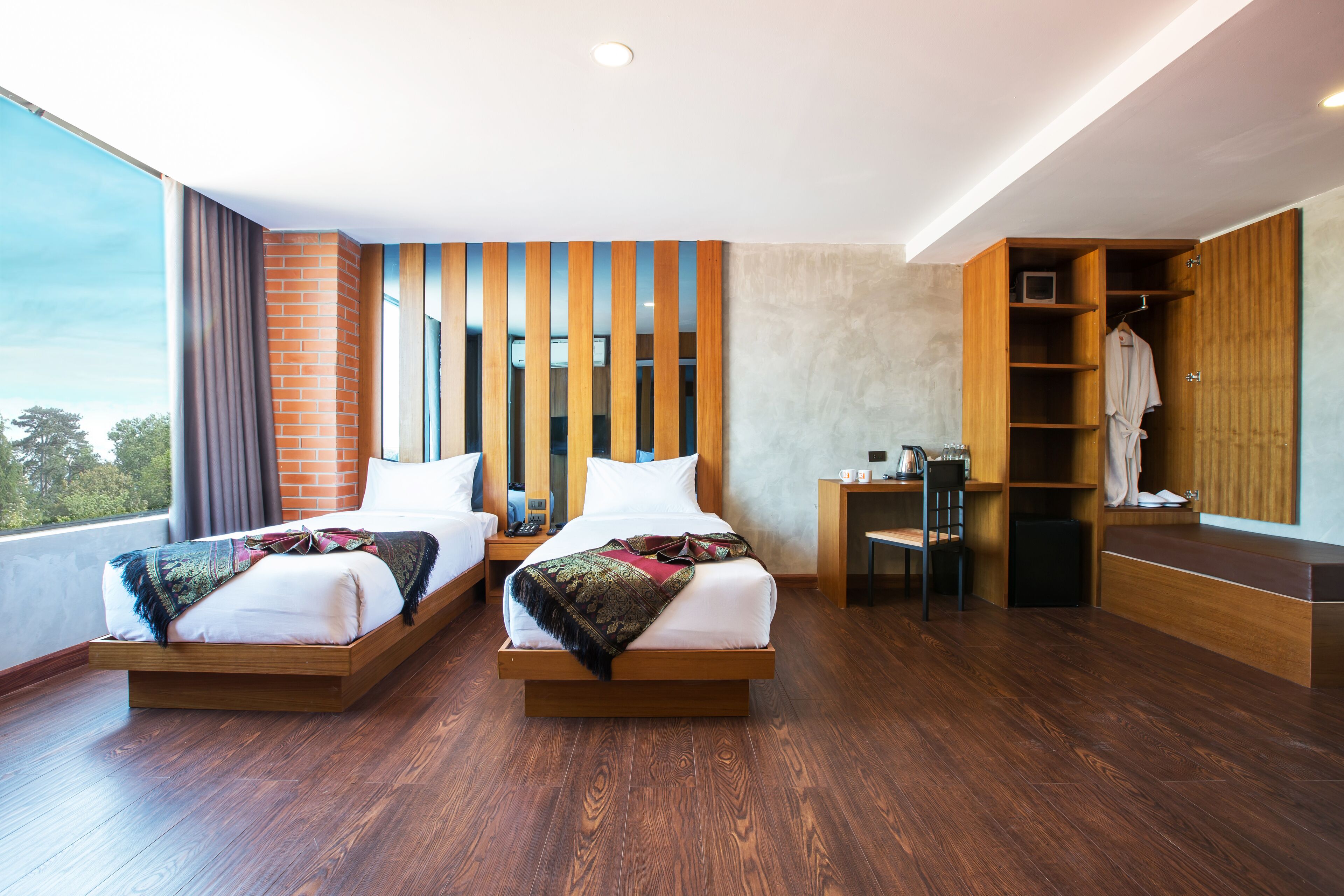 Una habitación de hotel moderna con dos camas, un armario de madera, un escritorio y un ventanal grande.