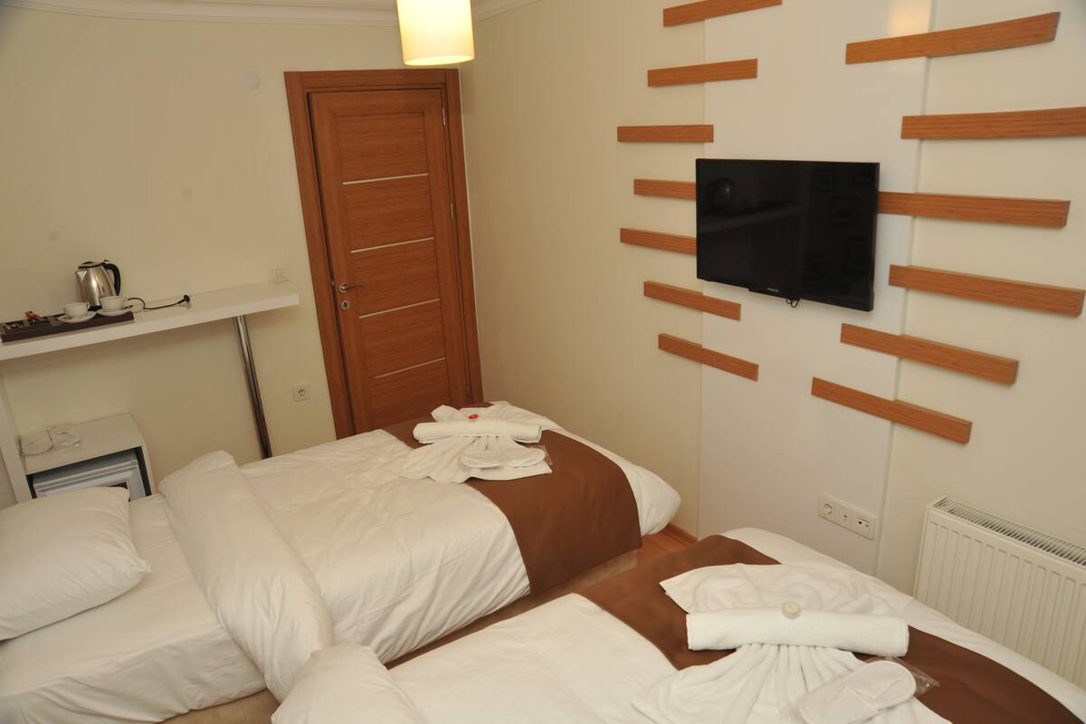 A hotel room with two beds, a TV mounted on the wall, a wooden shelf, and a door.
