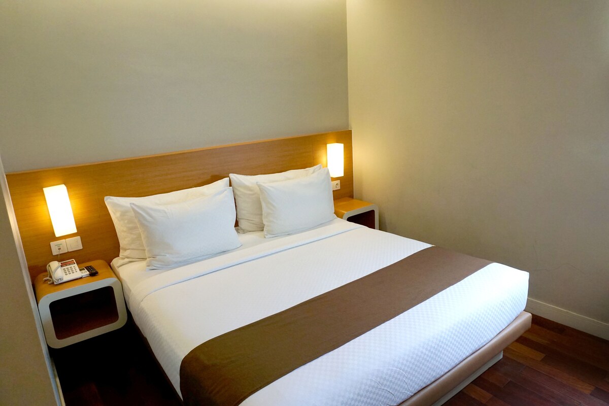A hotel room with a large bed, two bedside tables, a telephone, and wall-mounted lighting.