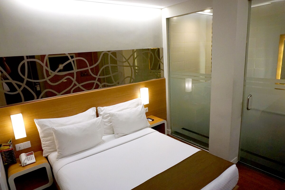 A hotel room with a bed, a bedside table with a phone, and a glass shower enclosure.