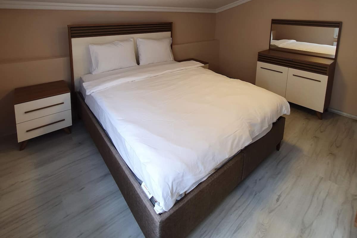 A bedroom with a large bed, a nightstand, a dresser, and a mirror.