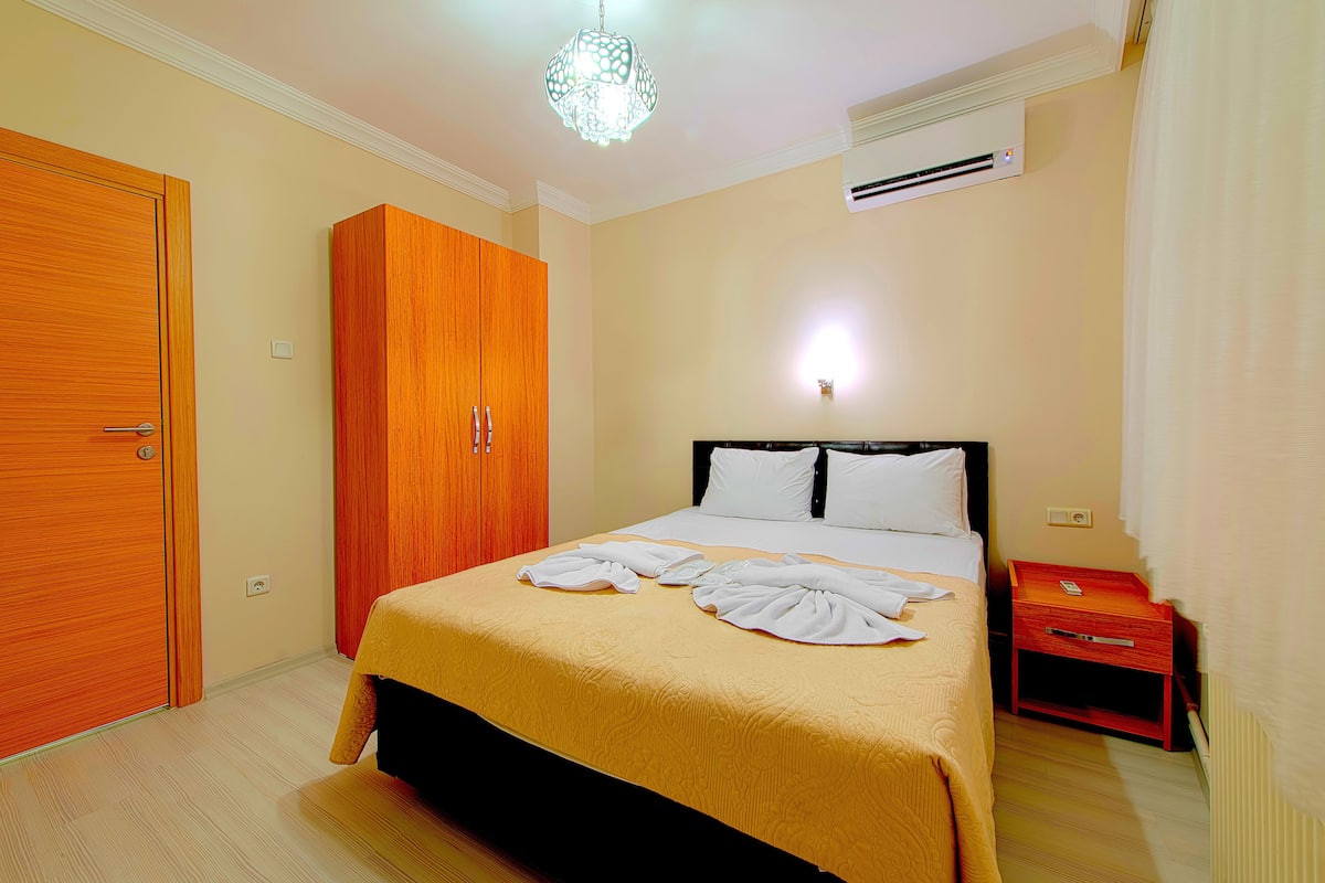 A hotel room with a bed, wardrobe, bedside table, and an air conditioning unit.
