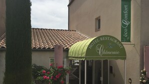 Entrada de hotel con toldo verde, un letrero que dice "Hotel Restaurant La Chènerie" y una pequeña ventana sobre la entrada.