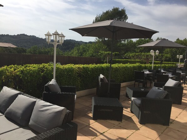 An outdoor patio area with wicker furniture, umbrellas, and a view of a landscaped garden.
