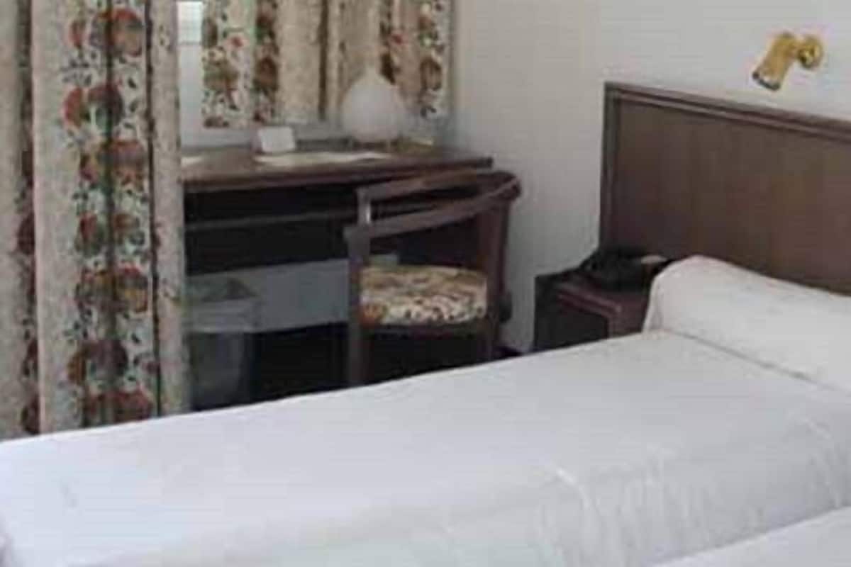 Une chambre d’hôtel avec deux lits simples, un bureau avec une chaise et une table de chevet avec une lampe.