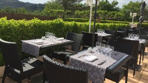 Un área de comedor al aire libre con mesas y sillas, rodeada de vegetación y vistas a las colinas.