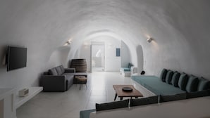 A modern, open-plan living space with a vaulted ceiling, a flat-screen TV mounted on the wall, a sofa, a coffee table, and a small side table. - White Concept Caves (Santorini)