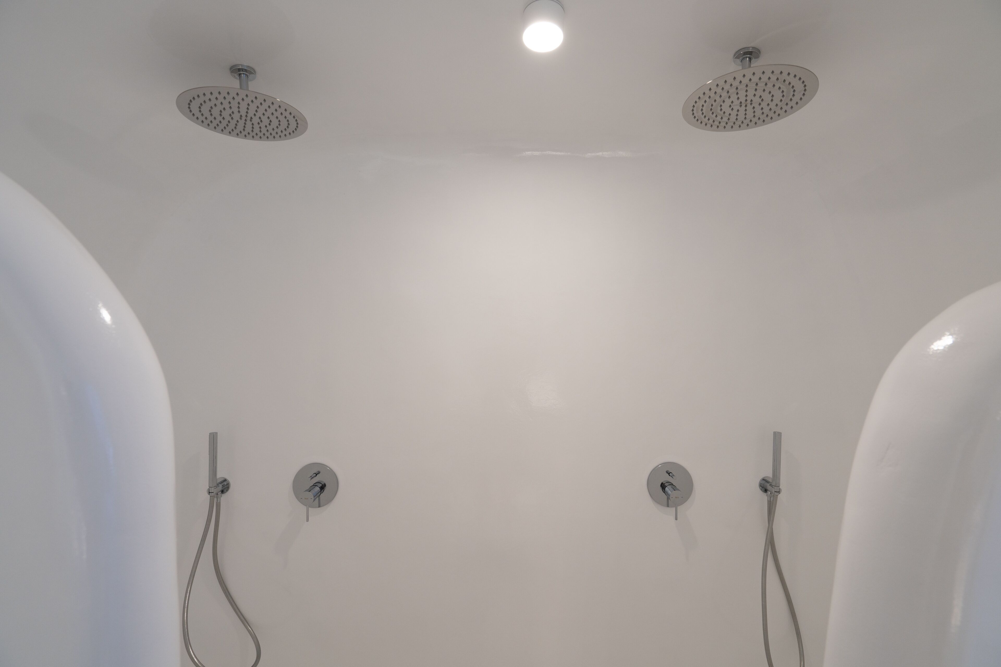 A modern bathroom with two overhead showerheads and two wall-mounted faucets.