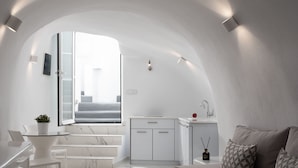 A modern, minimalist interior with a white color scheme, featuring a dining area, kitchen, and living space with a curved ceiling and built-in lighting. - White Concept Caves (Santorini)