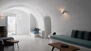 A modern, minimalist living room with a curved ceiling, a sofa with cushions, a small wooden table, and a bench with cushions. - White Concept Caves (Santorini)