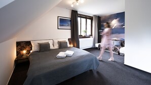 A modern hotel room with a large bed, a nightstand, a window with curtains, and a wall-mounted light fixture. - Penzion Sileo (Pribylina)