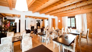 A spacious dining area with wooden beams, white patterned chairs, and a large window providing natural light. - Penzion Sileo (Pribylina)