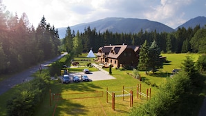 A lodge with a large deck, a tennis court, and a parking area with cars. - Penzion Sileo (Pribylina)