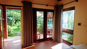 Una habitación con cama, una puerta de madera que da a un balcón y vista a una piscina.