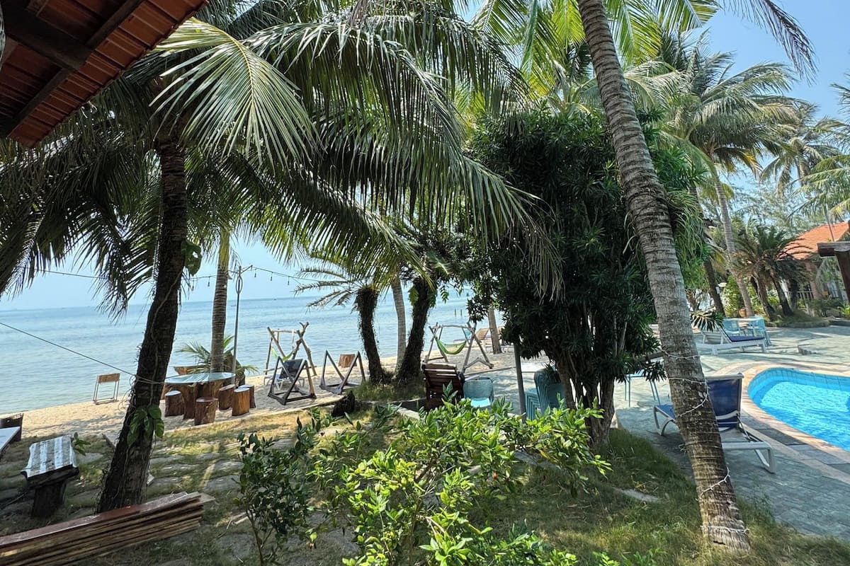 A beachside resort with a pool, palm trees, and a covered seating area.