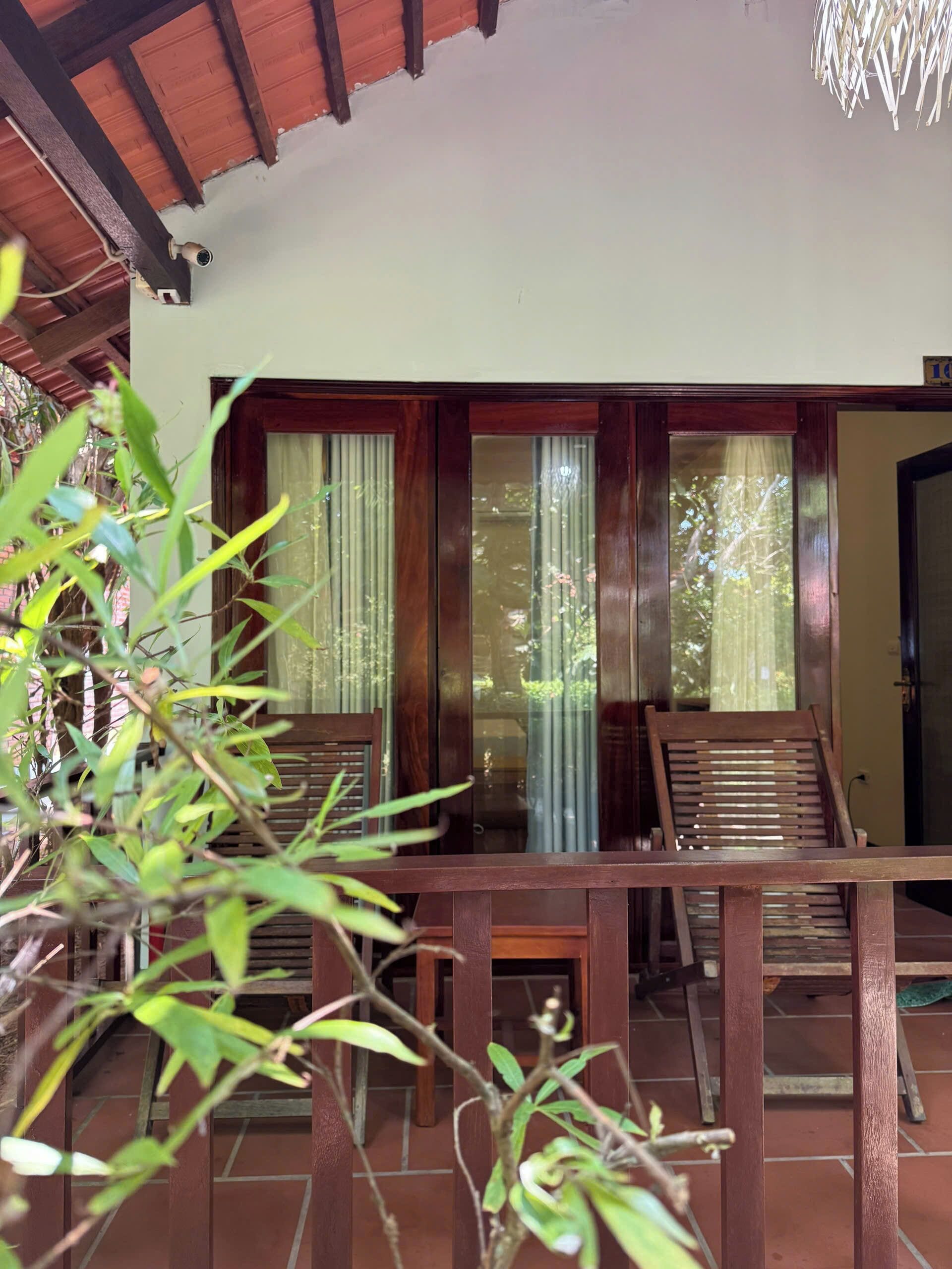 A wooden-framed room with a tiled floor, a wooden bench, and a view through a window with curtains.