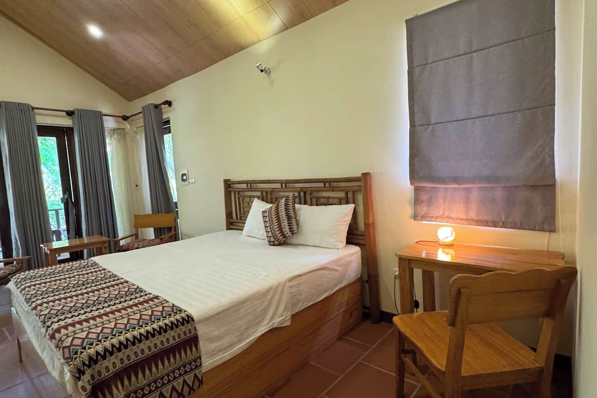 A bedroom with a wooden ceiling, a bed with patterned bedding, a nightstand, a chair, and a window with curtains.