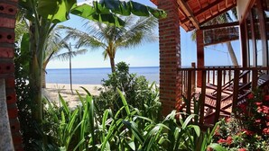 Vista a la playa a través de una estructura de ladrillo con barandilla de madera, palmeras y cielo despejado.