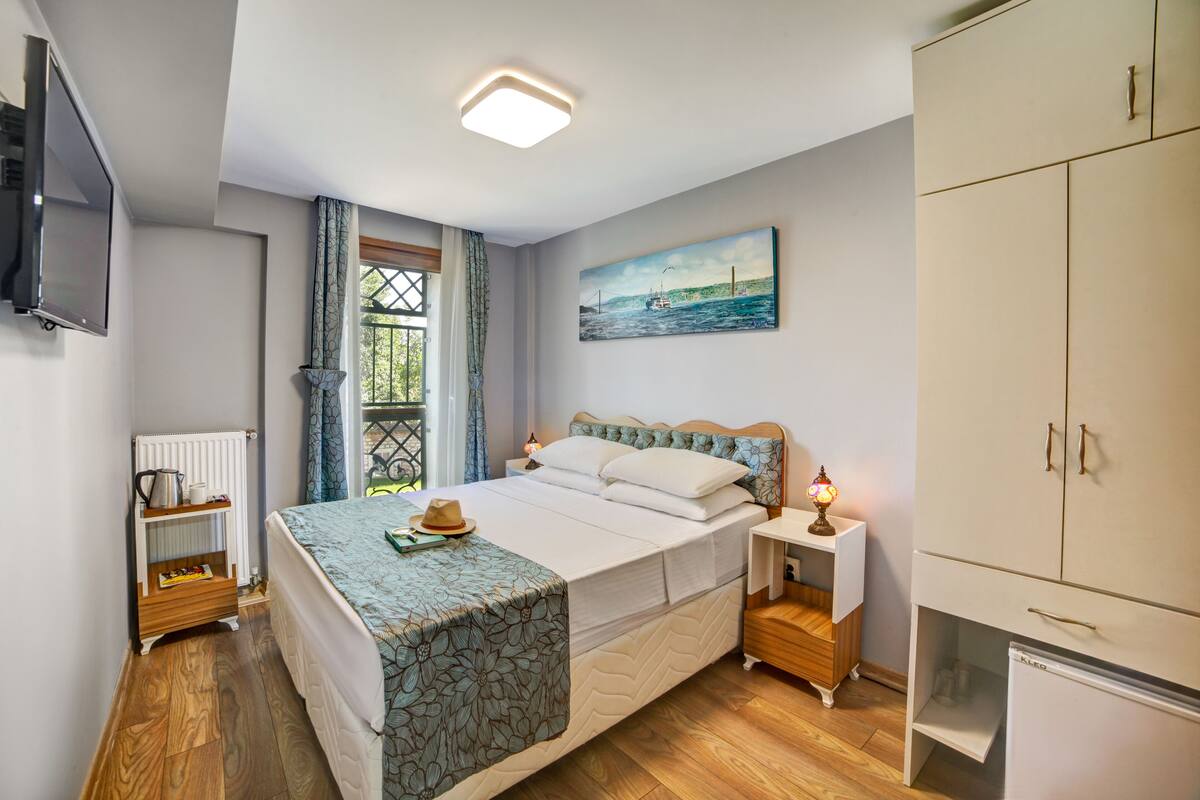 A bedroom with a bed, a nightstand, a wardrobe, a radiator, a television, and a window with curtains.