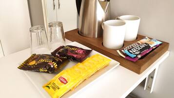 A kitchen counter with a coffee maker, two mugs, a kettle, and various snack packets.