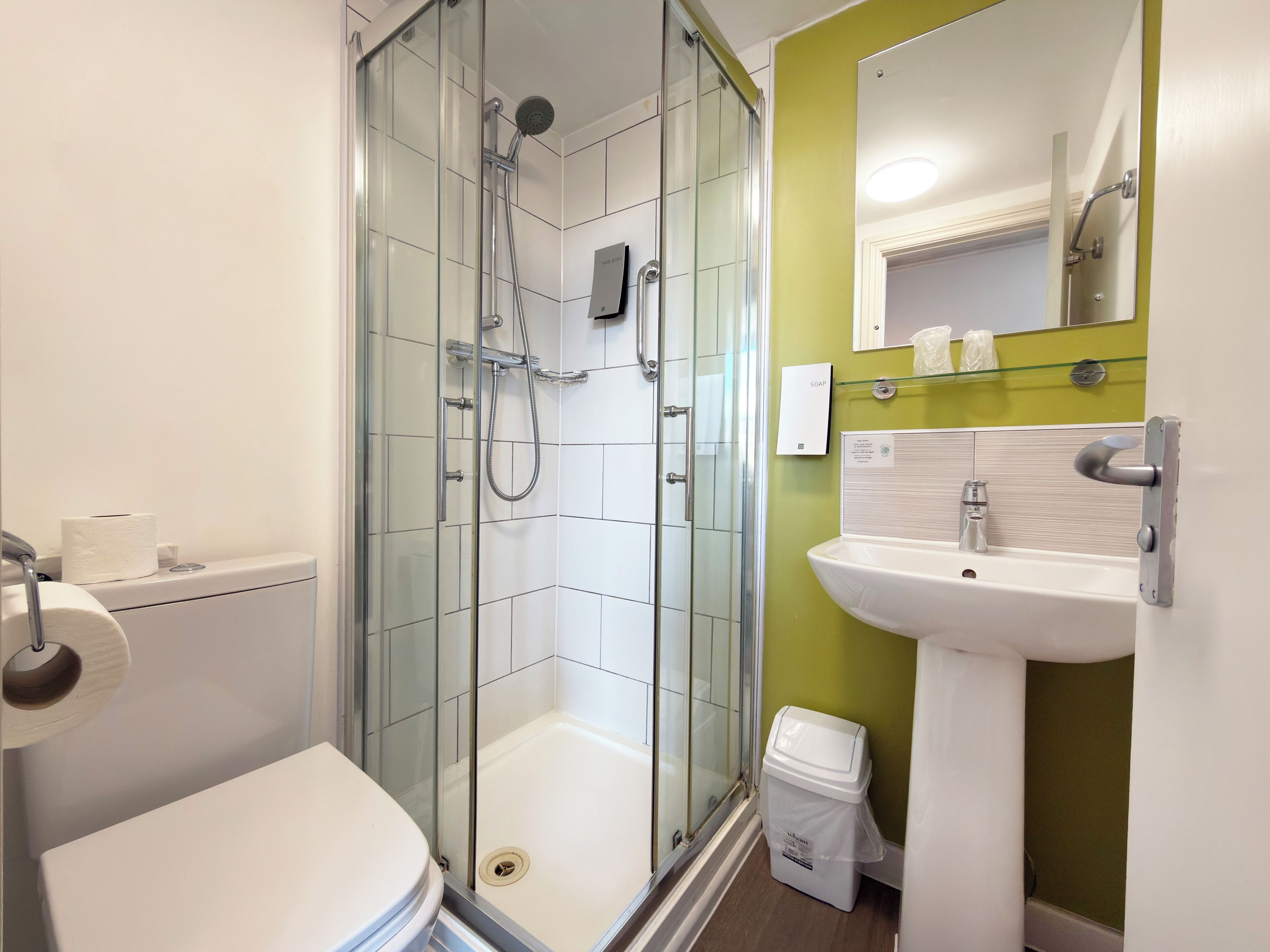 Un baño moderno con ducha de vidrio, inodoro blanco, lavamanos con espejo y un cubo de basura.