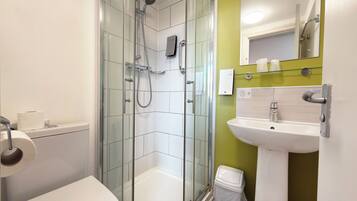 Un baño moderno con ducha de vidrio, inodoro blanco, lavamanos con espejo y un cubo de basura.