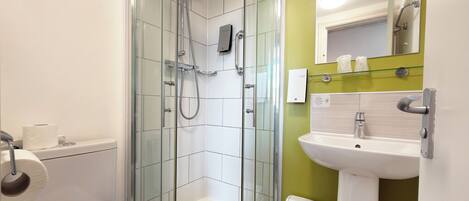 Un baño moderno con ducha de vidrio, inodoro blanco, lavamanos con espejo y un cubo de basura.