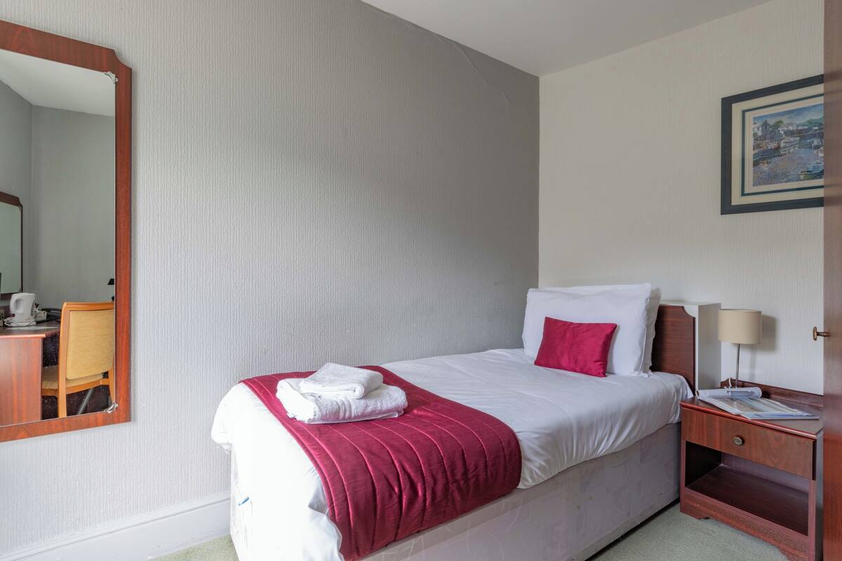 Een hotelkamer met een bed, nachtkastje, lamp, spiegel en een schilderij aan de muur.