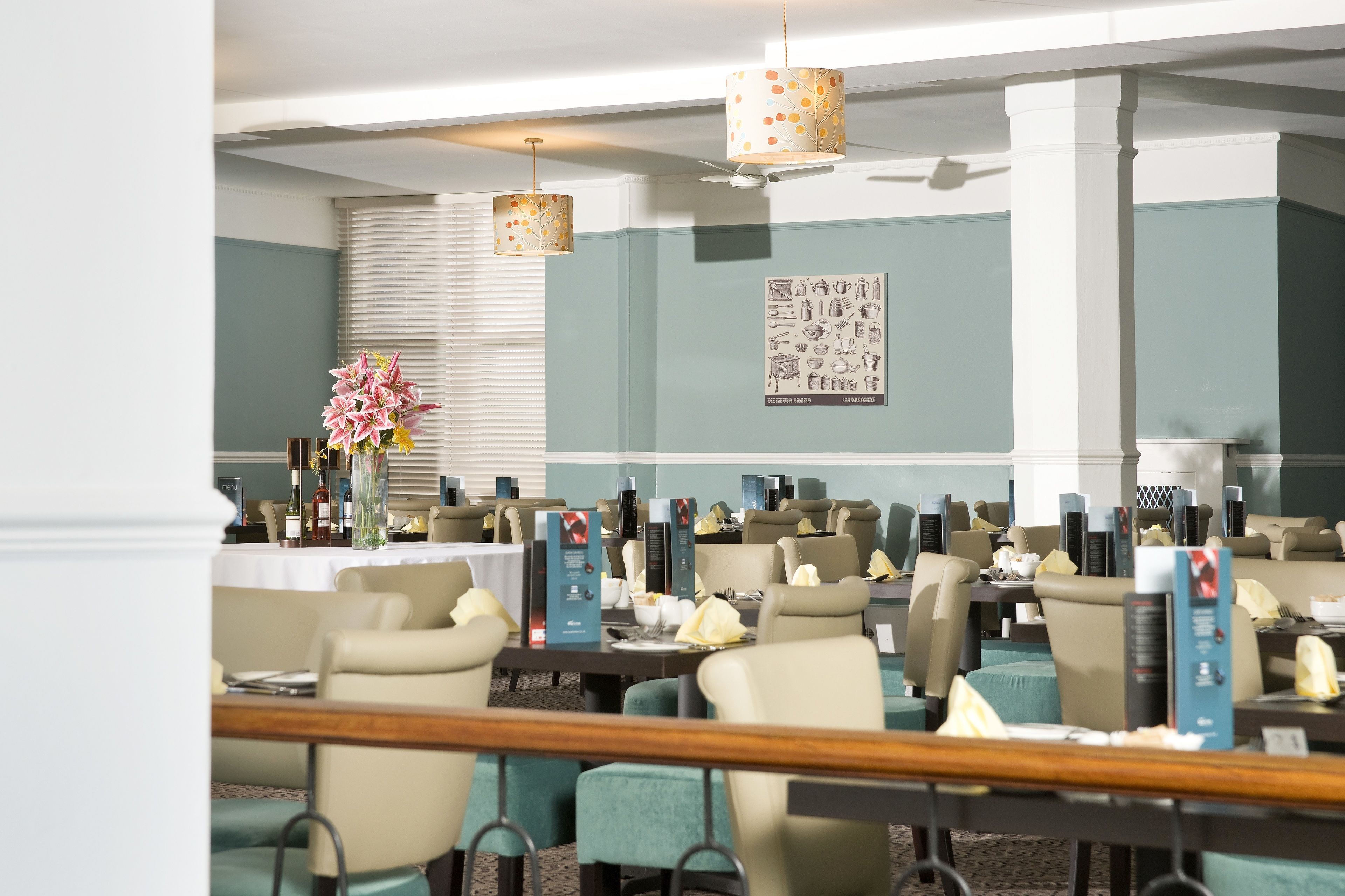 Une salle à manger d’hôtel avec plusieurs tables, des chaises et un ventilateur de plafond.