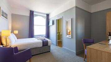 Habitación de hotel con cama, escritorio, silla, televisión y baño visible a través de una puerta abierta.