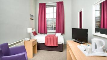 A hotel room with a bed, a desk, a chair, a television, and a window with curtains.