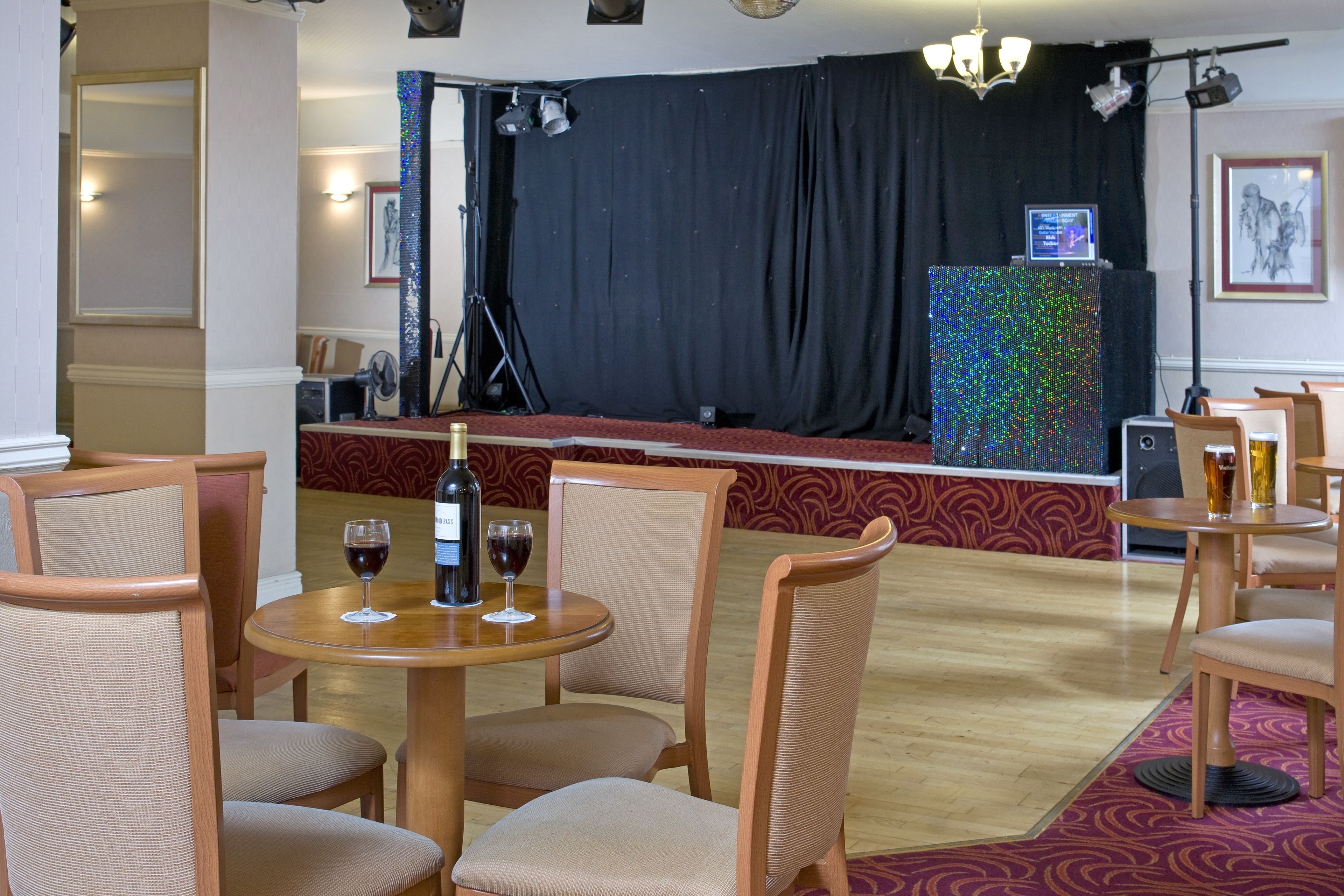 A restaurant with round tables and cushioned chairs, a stage with a black backdrop, and a colorful LED screen.