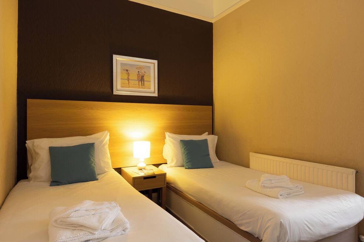 Een hotelkamer met twee bedden, een nachtkastje, een lamp en een lijst met een afbeelding aan de muur.