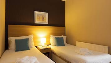 A hotel room with two beds, a nightstand, a lamp, and a framed picture on the wall.
