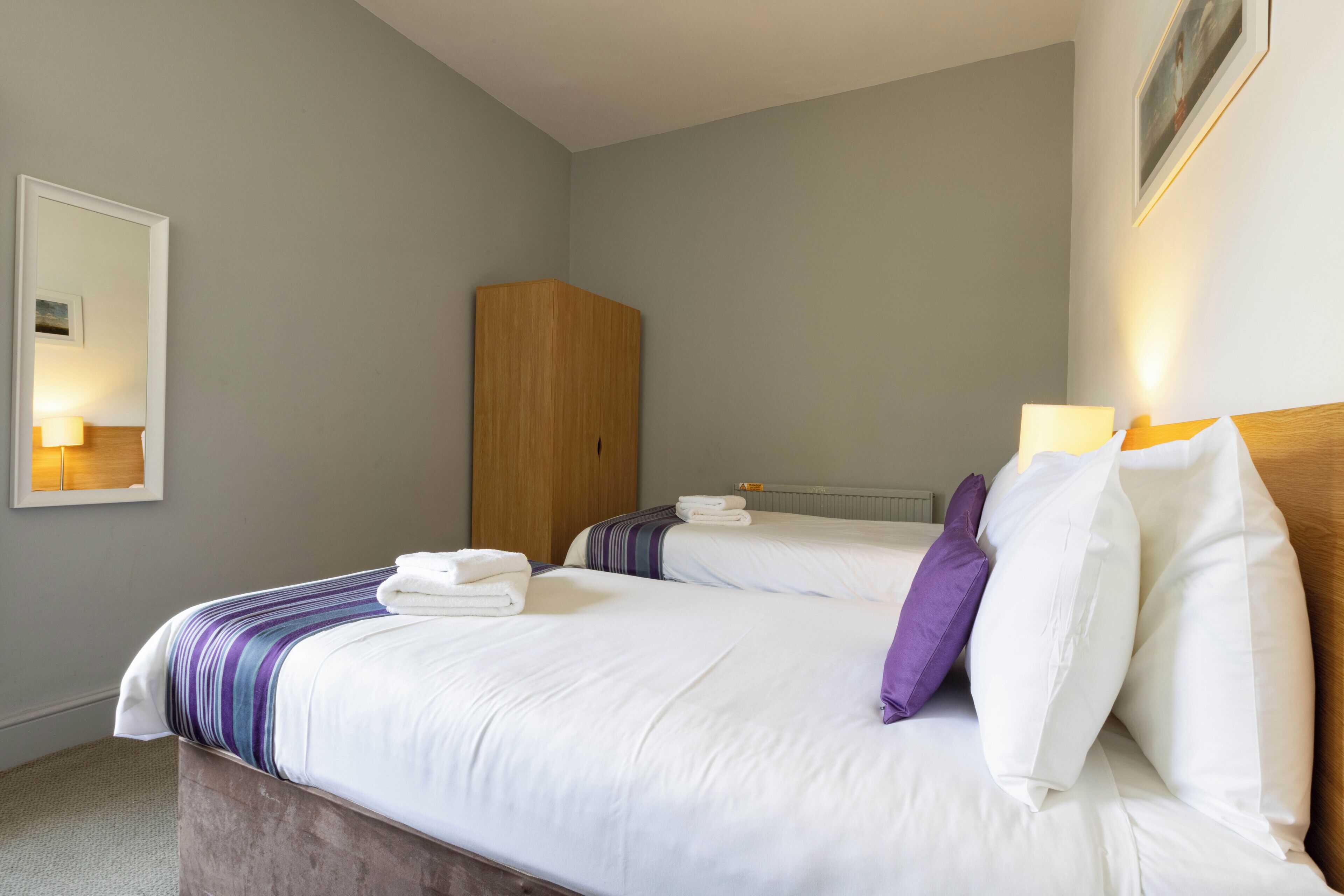 A hotel room with two beds, a wooden wardrobe, and a framed picture on the wall.