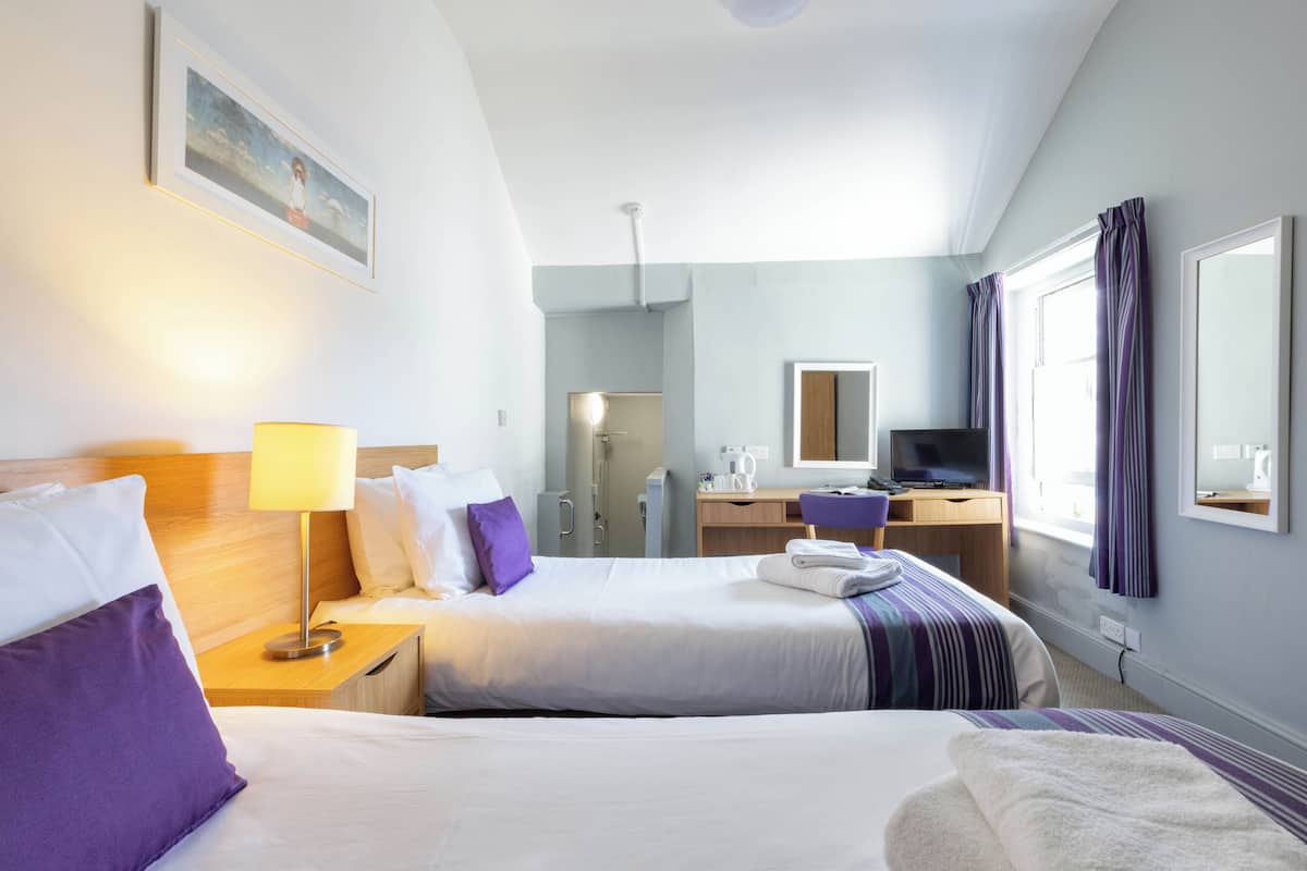 Een hotelkamer met twee bedden, een bureau, een televisie en een zichtbare badkamer door een open deur.
