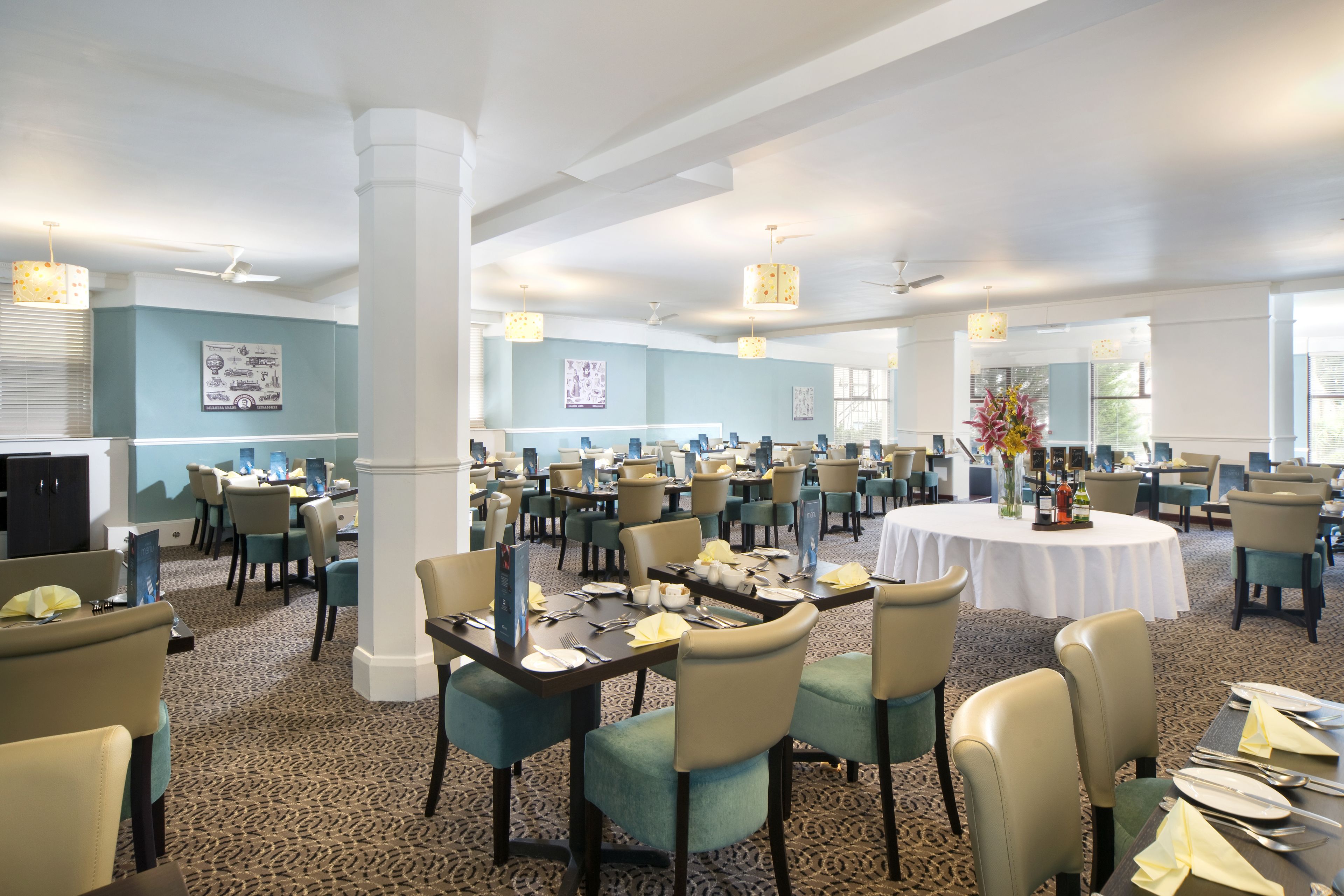 A spacious dining area with multiple tables and chairs, large windows, and ceiling fans.