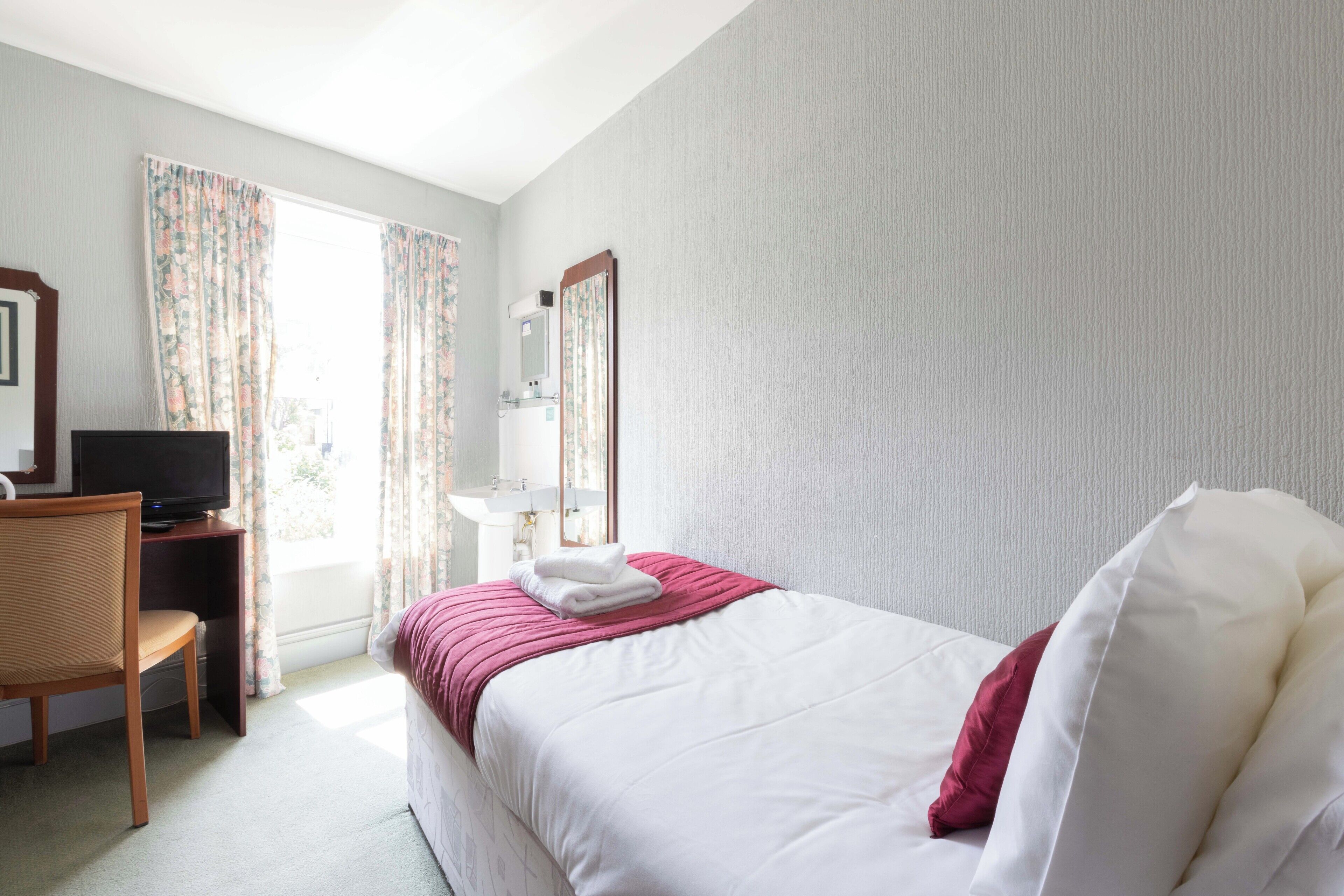 Een hotelkamer met een bed, een bureau met televisie, een badkamer met spiegel en gordijnen.