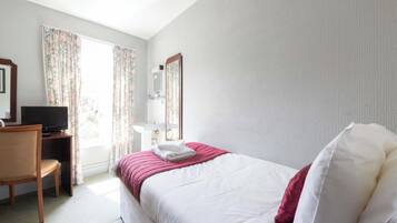 A hotel room with a bed, a desk with a television, a bathroom with a mirror, and curtains.